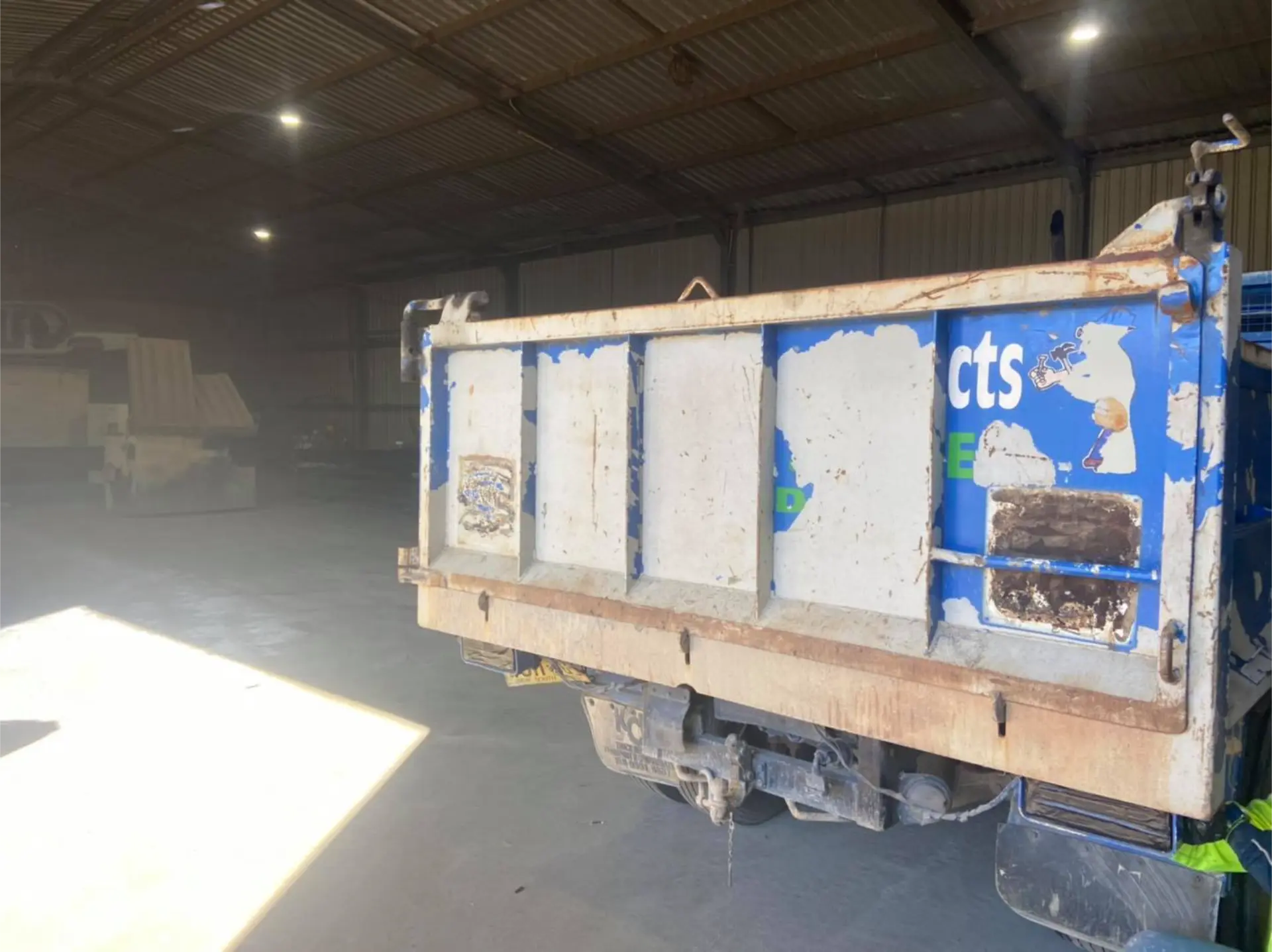 Rear of a blue tipper truck body with flaking, failed paint ready for stripping back